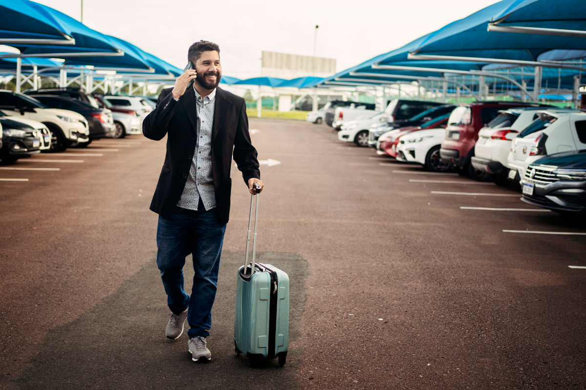 Traveler walking through airport parking lot with a rolling suitcase and talking on a phone