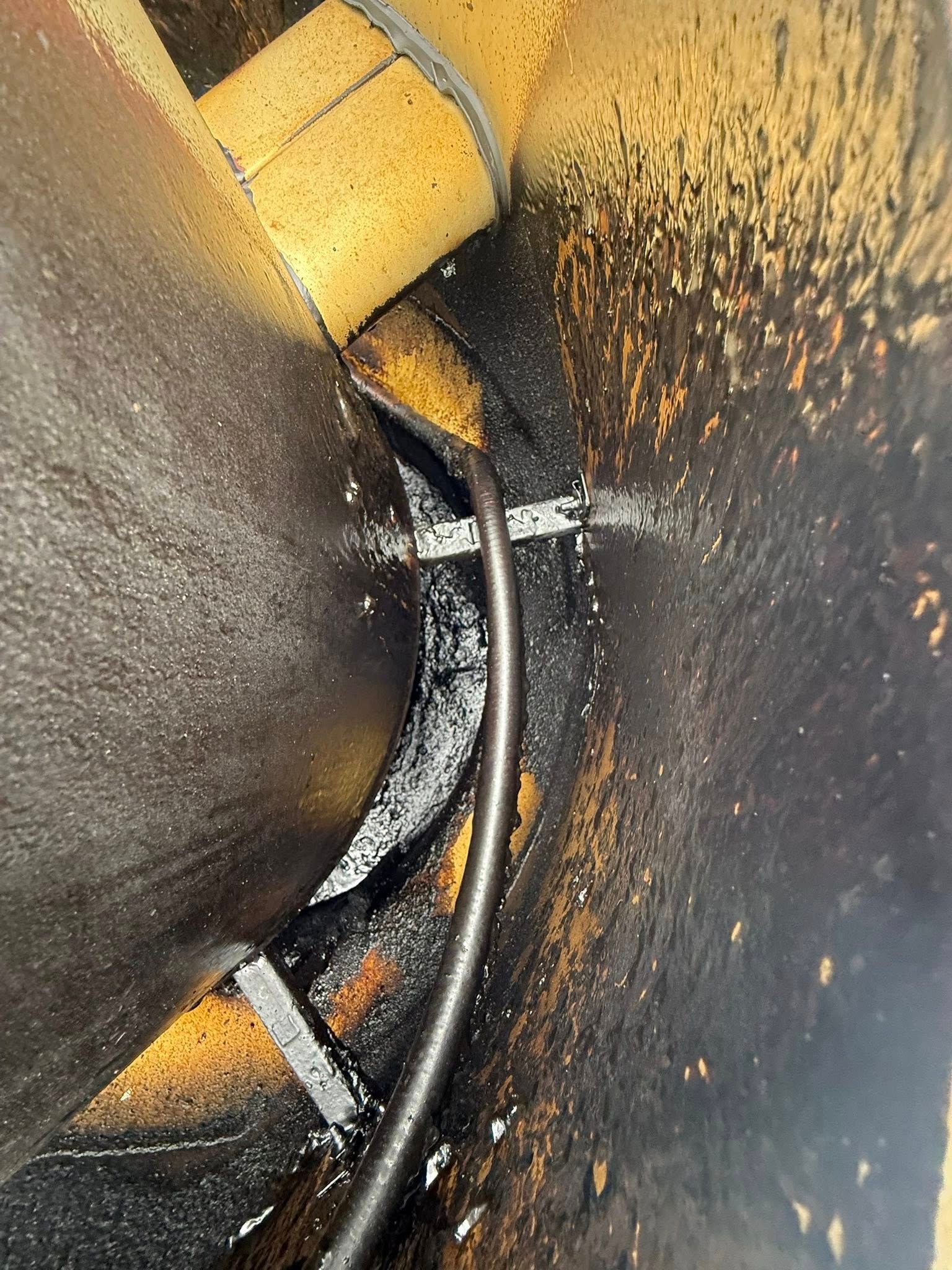 Close-up of a yellow and black curved metal surface with visible rust and a cable or hose running through it