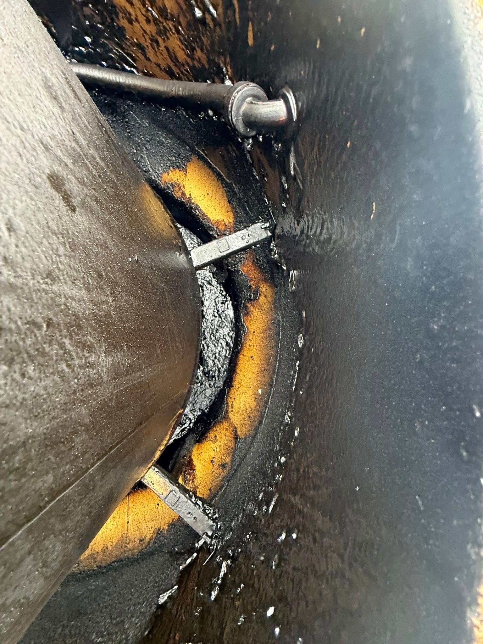 Close-up of a cracked metal surface with orange rust and black grime, showing damaged bolts and seams