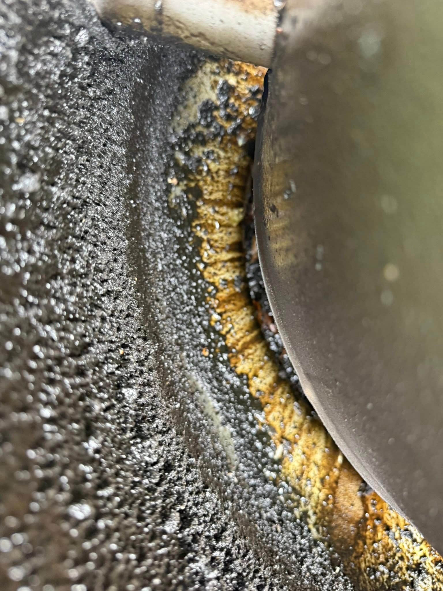 Close-up of a rusty, stained metal surface with gray speckling and a curved silver edge