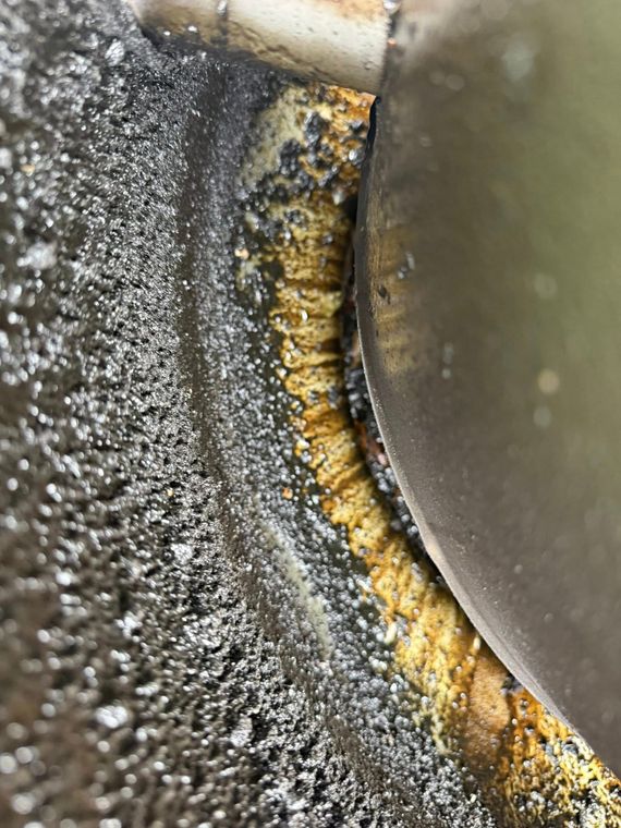 Close-up of a rusty, stained metal surface with gray speckling and a curved silver edge