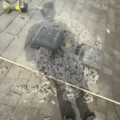 Roof shingles with a damaged vent and a pile of gray insulation around it