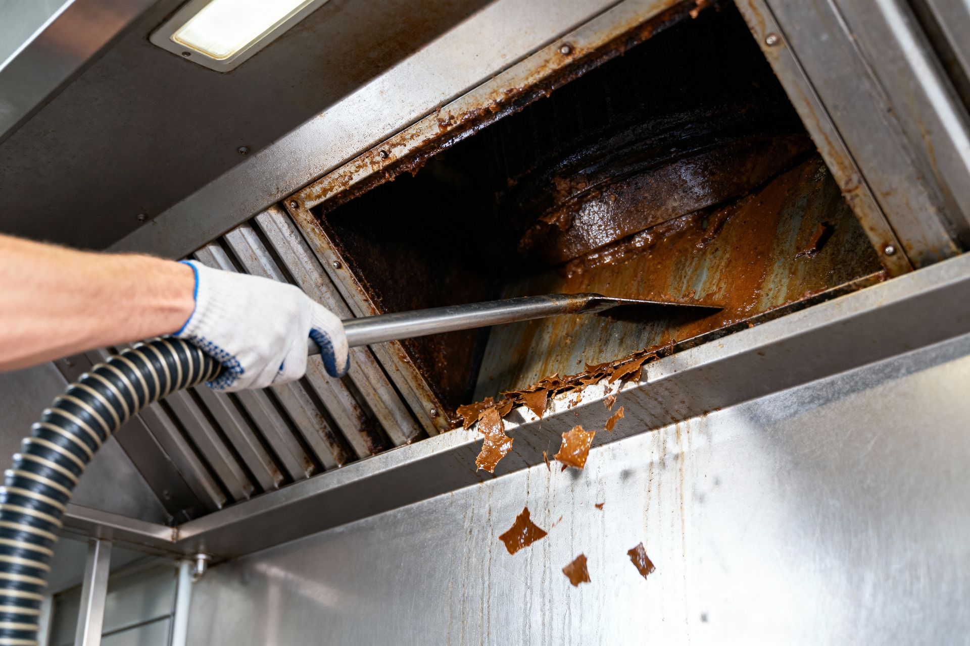 Hand using a metal scraper to clean grease from a stainless steel kitchen exhaust hood