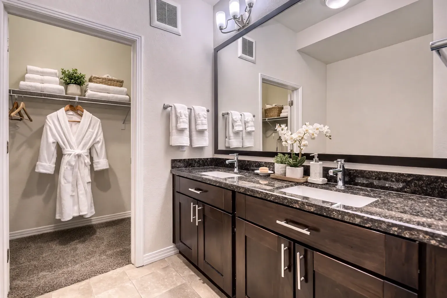 Bathroom vanity with dual sinks and a walk-in closet with a robe.