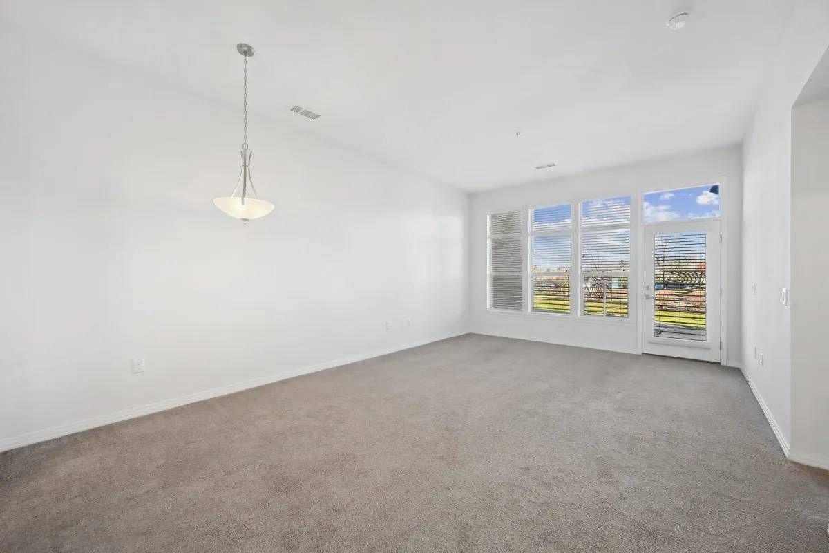 Empty living room with large windows and a glass door leading to a balcony.