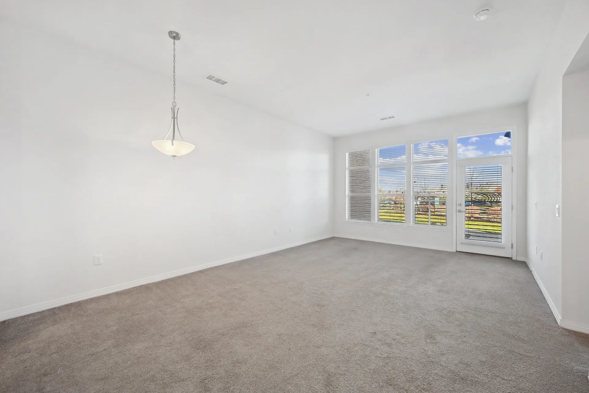 Empty living room with large windows and a glass door leading to a balcony.