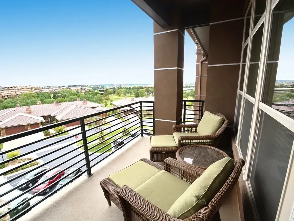 Balcony with wicker chairs and green cushions overlooking a sunny neighborhood view.