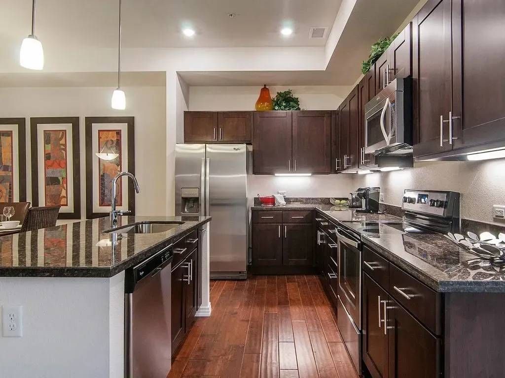 Modern kitchen with dark wood cabinets, granite countertops, stainless steel appliances, and hardwood floors.