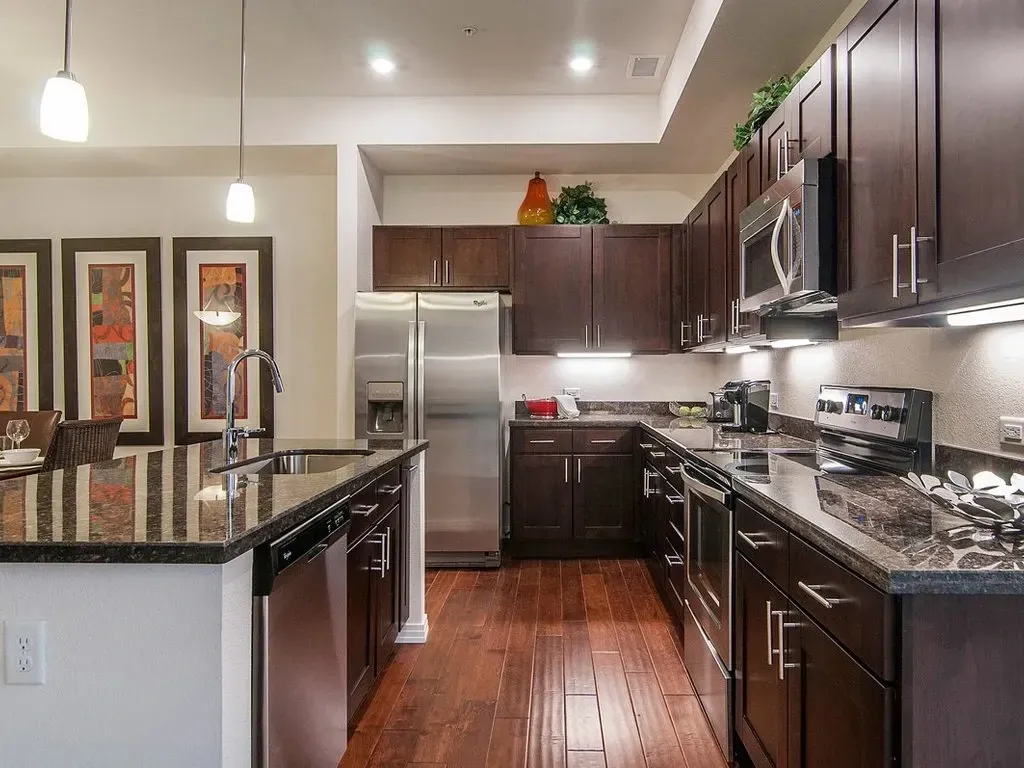 Modern kitchen with dark wood cabinets, granite countertops, stainless steel appliances, and hardwood floors.