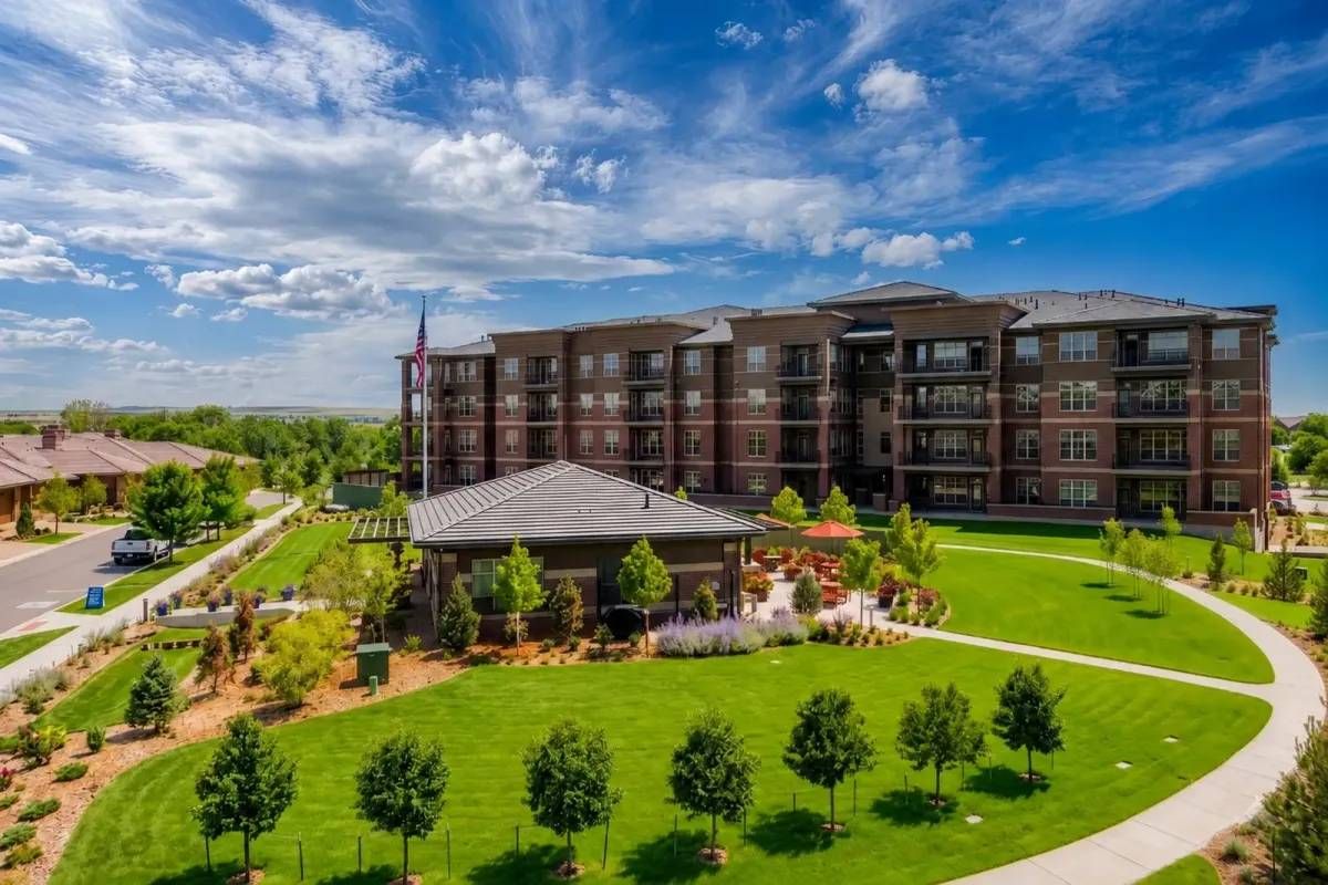 Modern apartment complex with landscaped green lawn, gazebo, and cloudy blue sky.