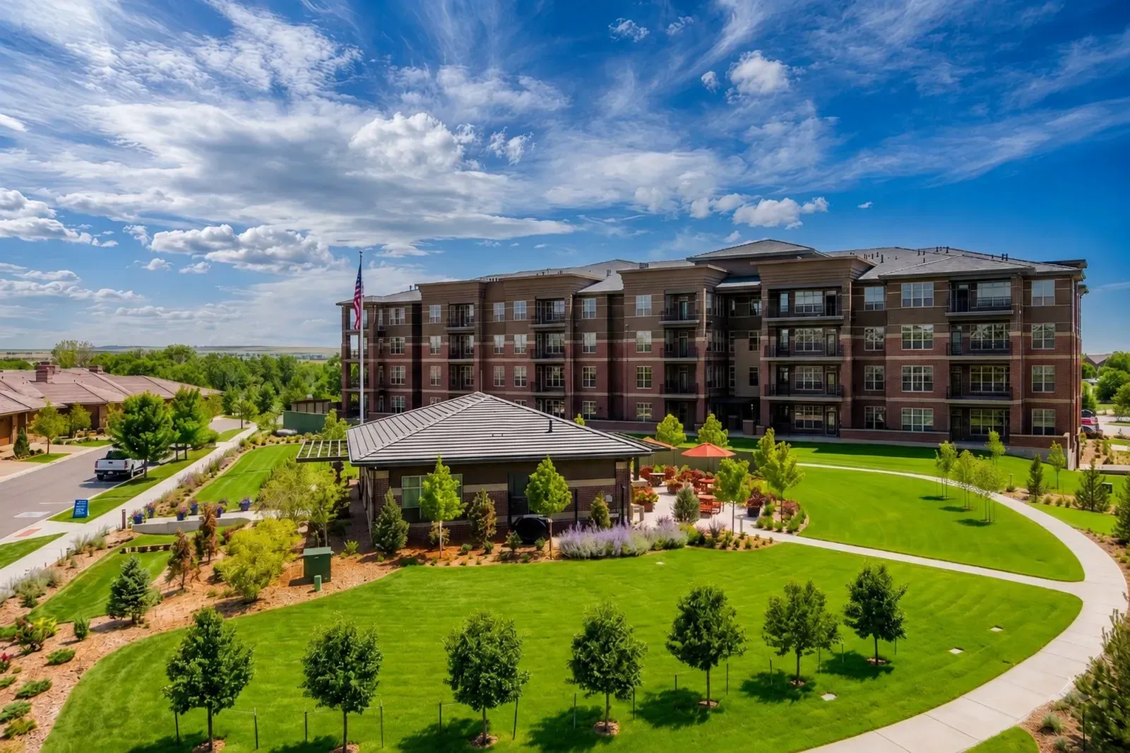 Modern apartment complex with a landscaped green lawn and covered entrance under a cloudy blue sky.