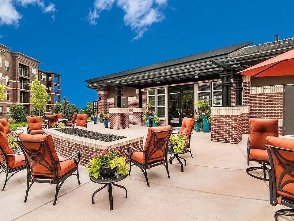 Rooftop patio with orange chairs, tables, and planters under a bright blue sky.