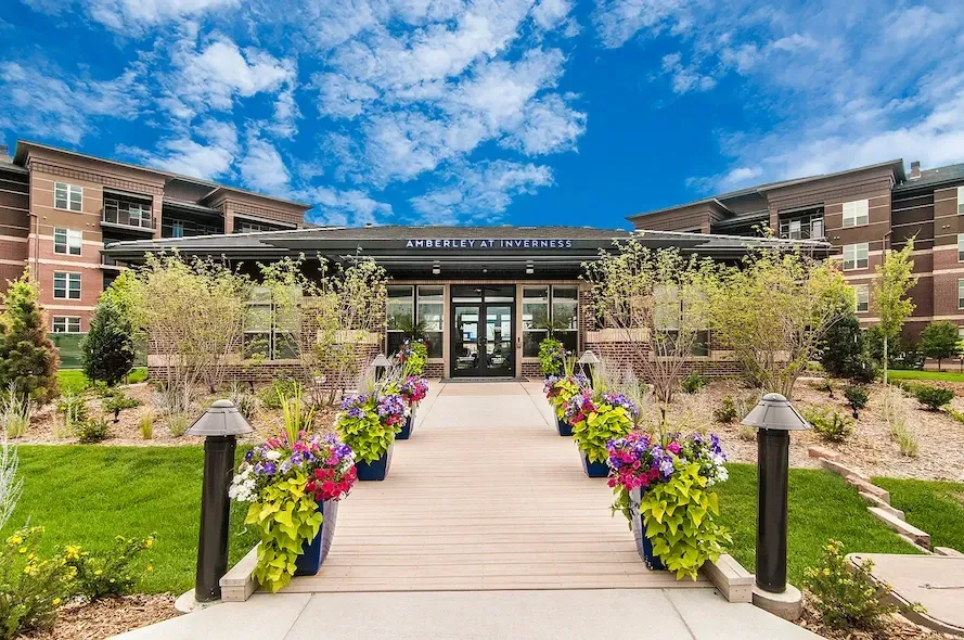 Landscaped walkway with colorful flowers leading to a modern building under a blue sky.