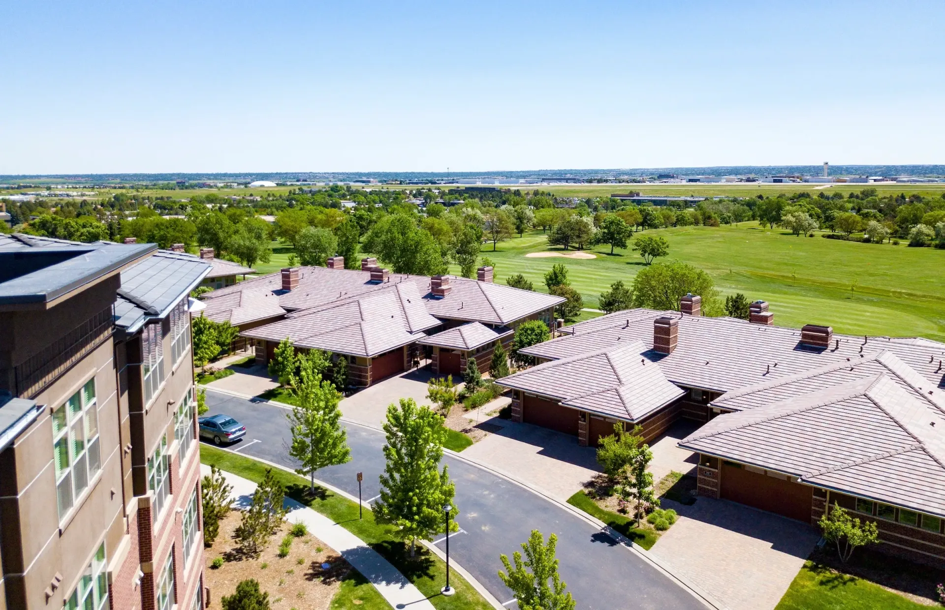 Aerial view of modern apartment buildings beside green fields under a clear sky.
