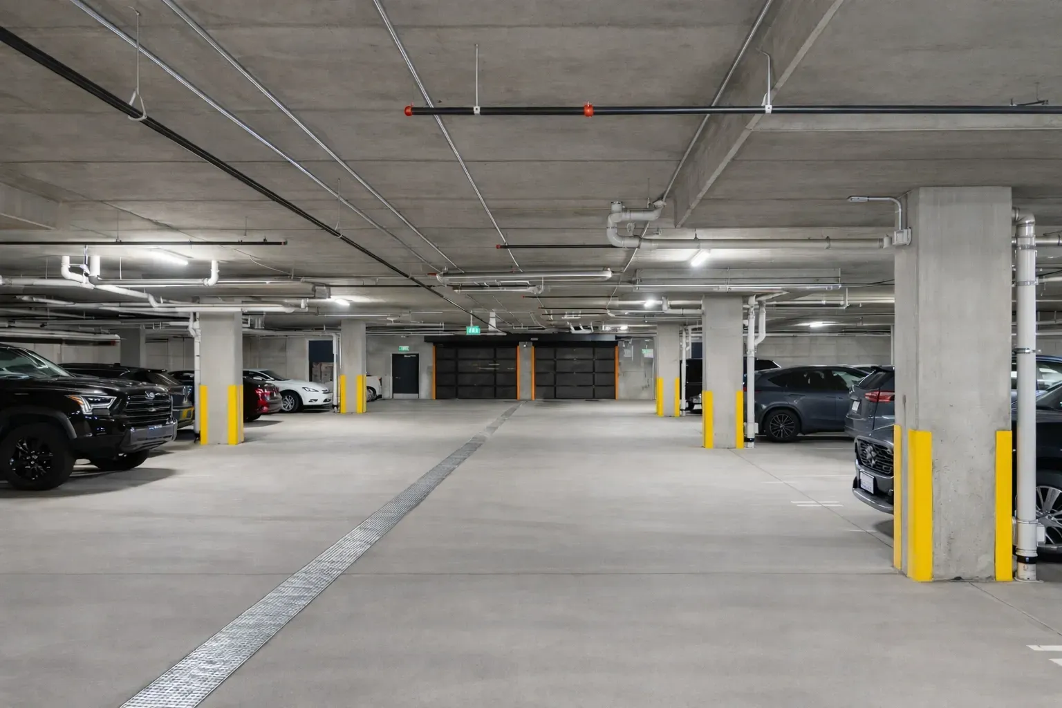 Empty underground parking garage with concrete pillars and parked cars on both sides.