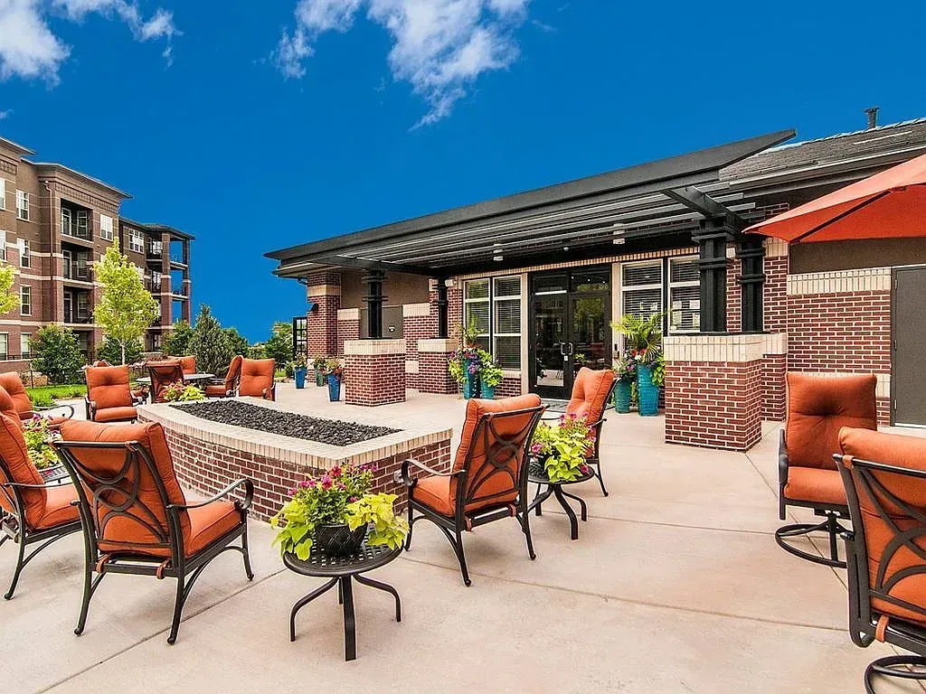 Outdoor terrace with empty tables, orange chairs, and a brick building under a blue sky.