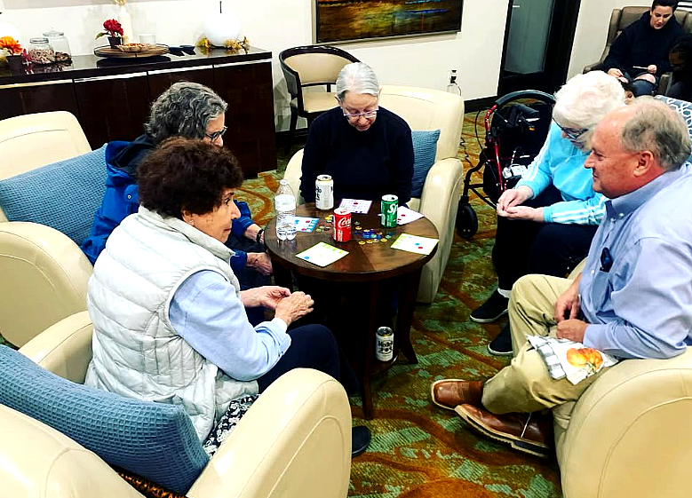 People seated in a lounge, chatting around a small table with drinks and cards.