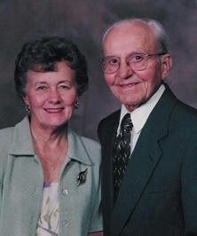 Portrait of a smiling couple in formal attire against a gray studio backdrop