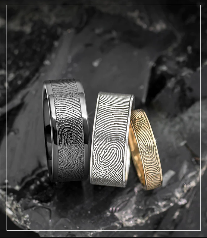 Three fingerprint-pattern rings in black, silver, and gold on a dark background
