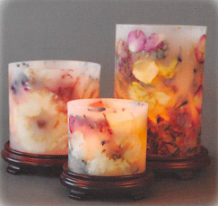 Three floral candle jars in soft white, peach, and amber tones on a dark surface