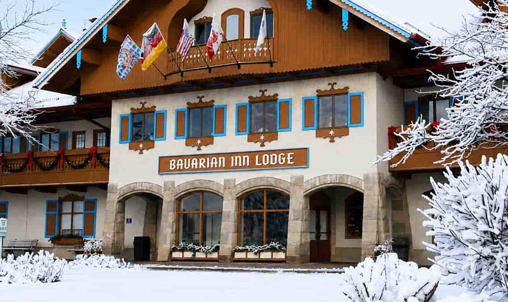 Snow-covered Bavarian-style hotel building with festive decorations and winter trees outside the Bavarian Inn Lodge.
