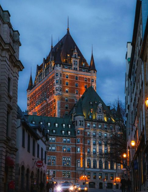 Illuminated Fairmont Le Château Frontenac rising above a historic Old Québec street at dusk.