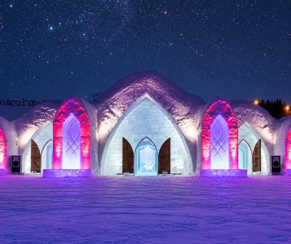Snow-covered entrance to Hôtel de Glace near Québec City, featuring arched ice walls and wooden doors.