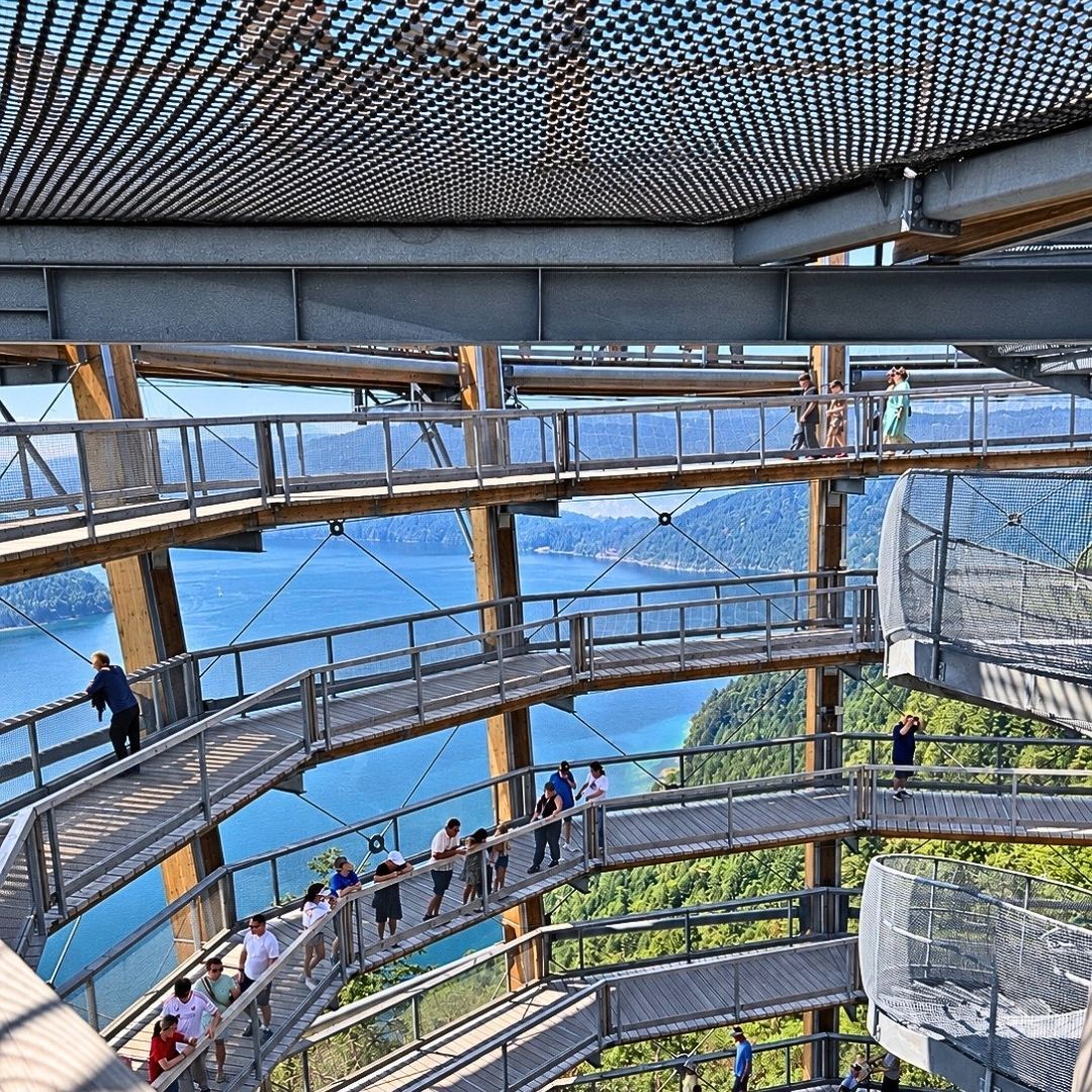 Visitors walking along the spiral observation tower at Malahat SkyWalk, overlooking Saanich Inlet and forested mountains on Vancouver Island, BC.