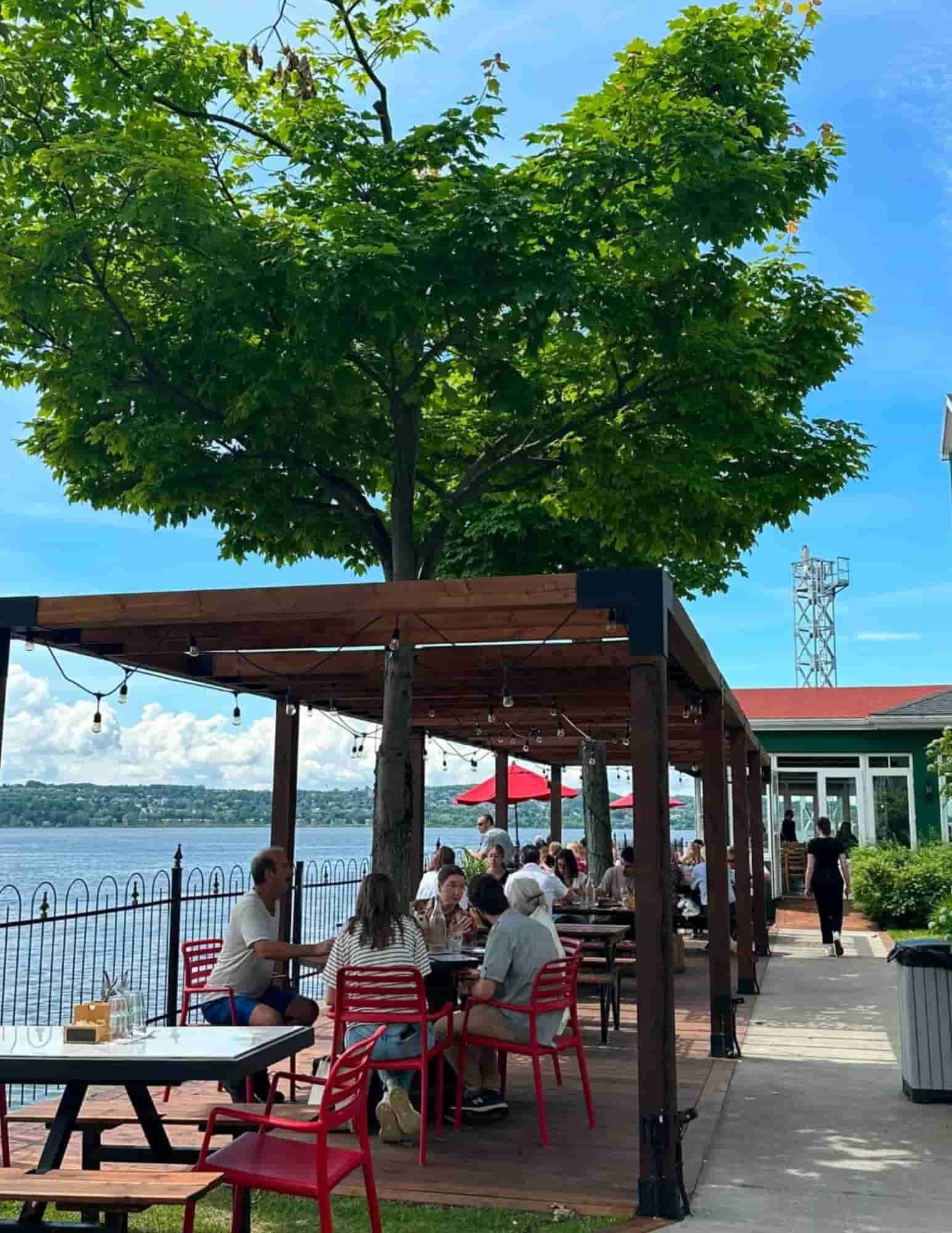 Guests enjoying lunch on the waterfront terrace at Auberge La Goéliche on Île d'Orléans, overlooking the St. Lawrence River near Québec City.