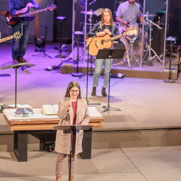 A group of people playing instruments on a stage including a woman singing into a microphone