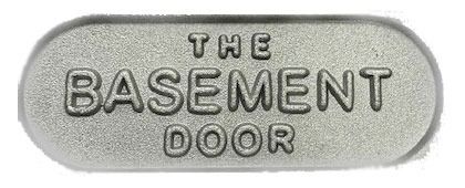 A silver, pill-shaped sign with the embossed text "THE BASEMENT DOOR".