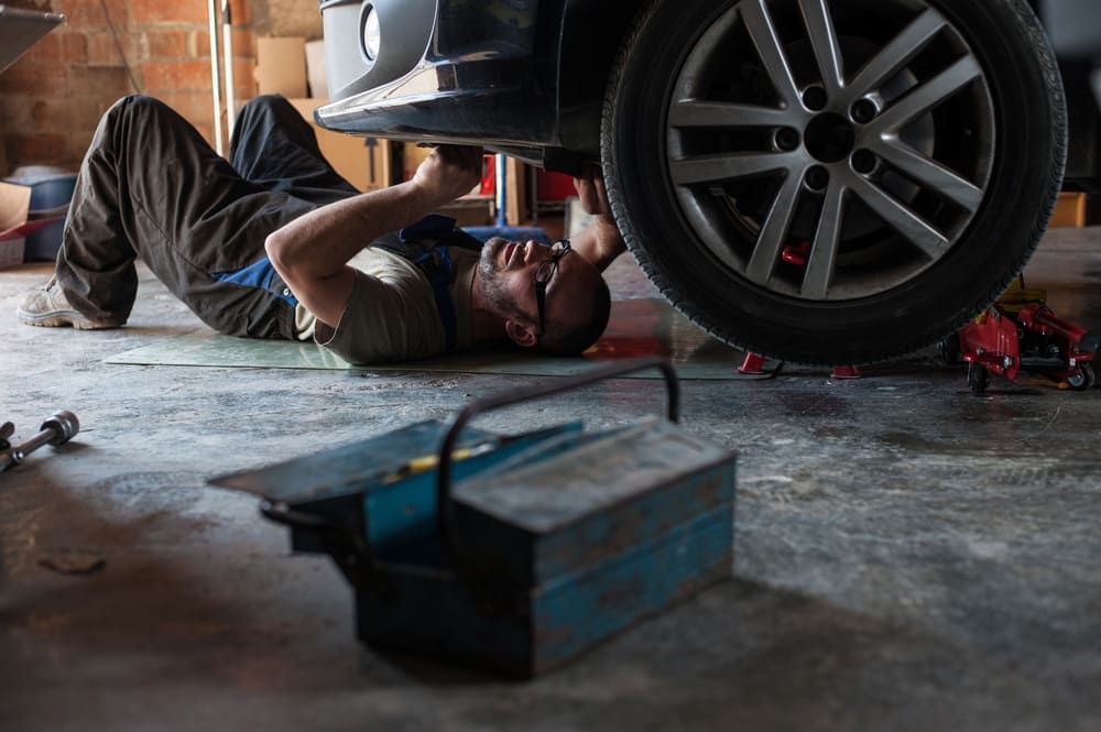 A Man Is Laying On The Ground Under A Car In A Garage — Automotive Repair Centre In Garbutt, QLD
