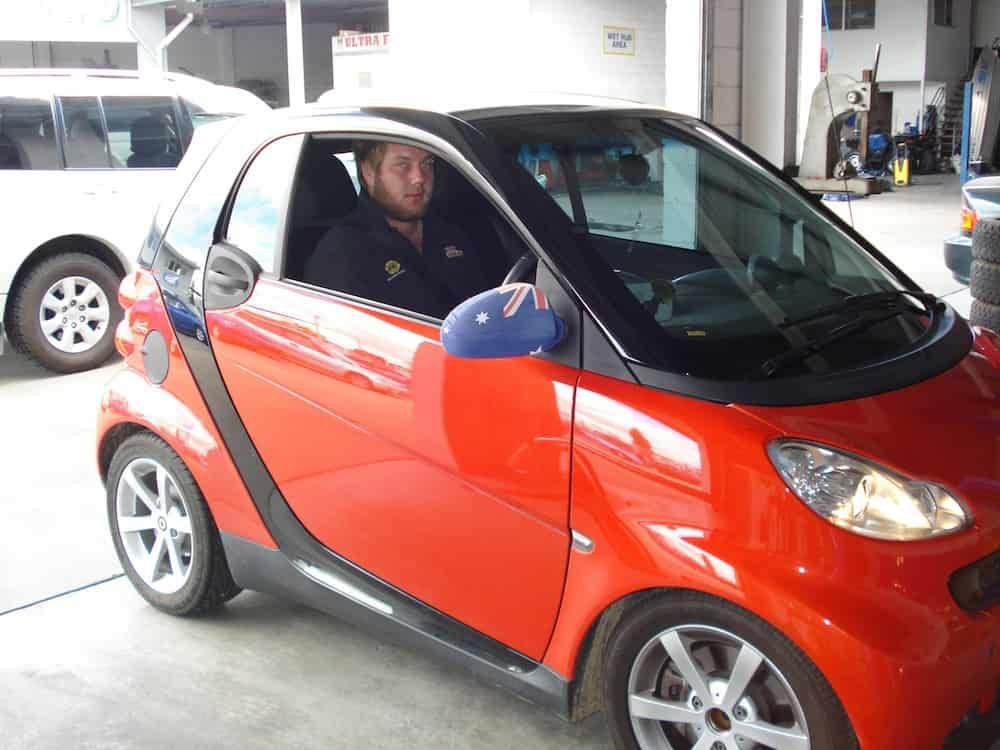 A Man Is Sitting In A Red Smart Car — Automotive Repair Centre In Garbutt, QLD