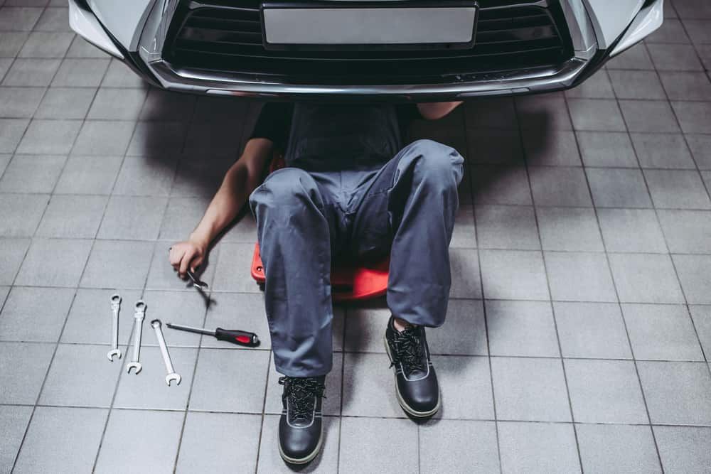 A Man Is Sitting Under A Car In A Garage — Automotive Repair Centre In Garbutt, QLD