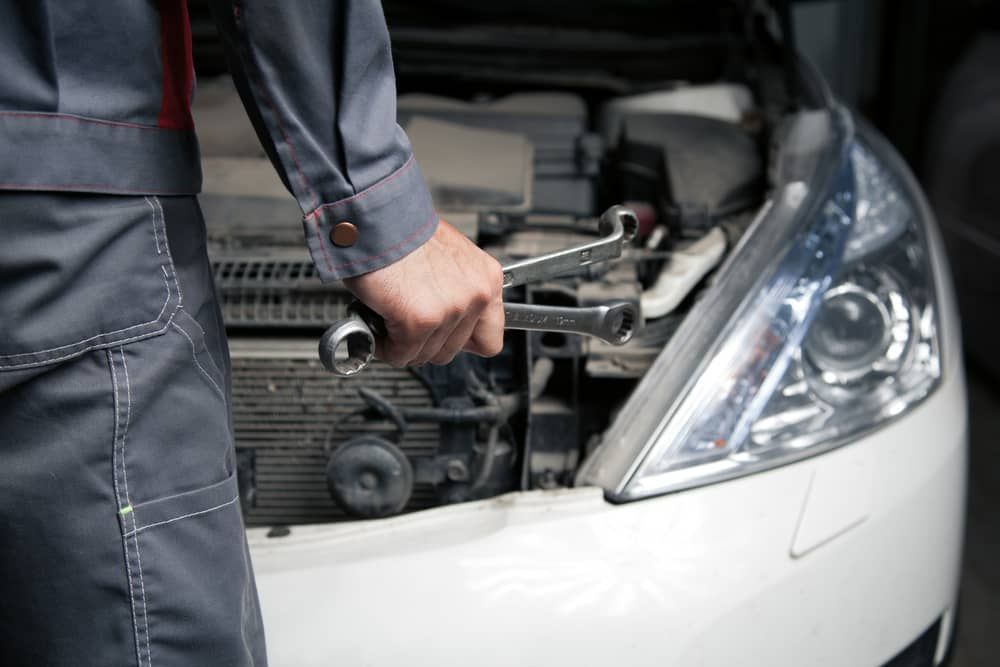 A Mechanic Is Holding A Wrench In Front Of A Car With The Hood Open — Automotive Repair Centre In Garbutt, QLD