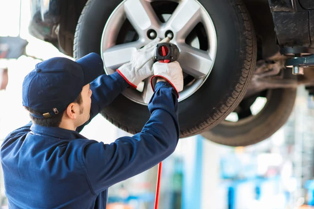 A Man Is Changing A Tire On A Car In A Garage — Automotive Repair Centre In Garbutt, QLD
