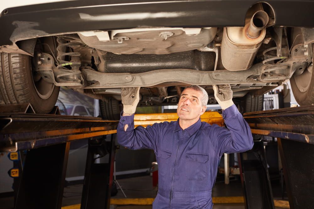 A Man Is Working Under A Car On A Lift In A Garage — Automotive Repair Centre In Garbutt, QLD