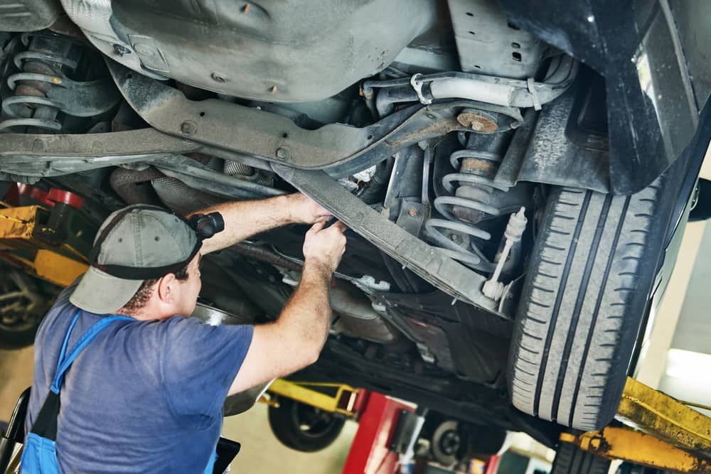 A Man Is Working Underneath A Car In A Garage — Automotive Repair Centre In Garbutt, QLD