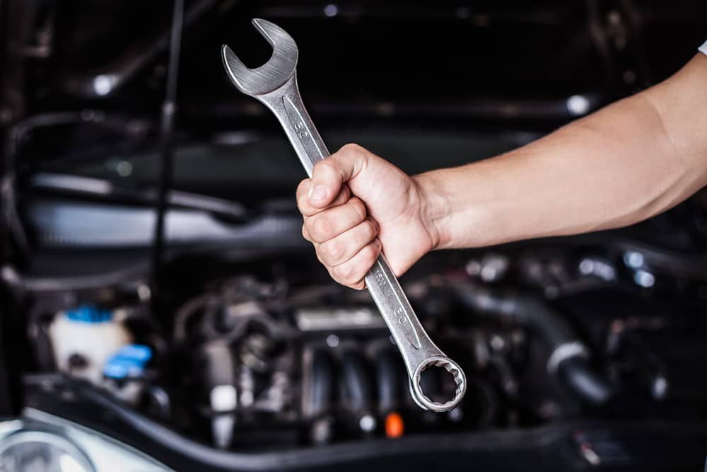 A Person Is Holding A Wrench In Front Of A Car Engine — Automotive Repair Centre In Garbutt, QLD