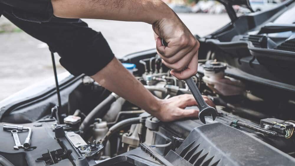 A Man Is Working On The Engine Of A Car With A Wrench — Automotive Repair Centre In Garbutt, QLD