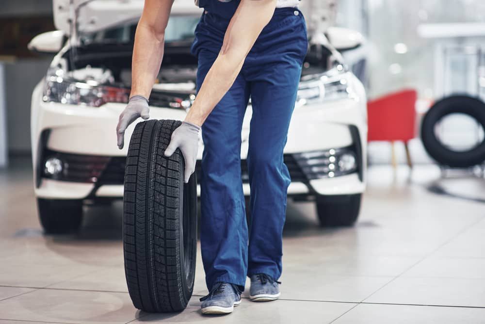 A Man Is Holding A Tire In Front Of A Car In A Garage — Automotive Repair Centre In Garbutt, QLD