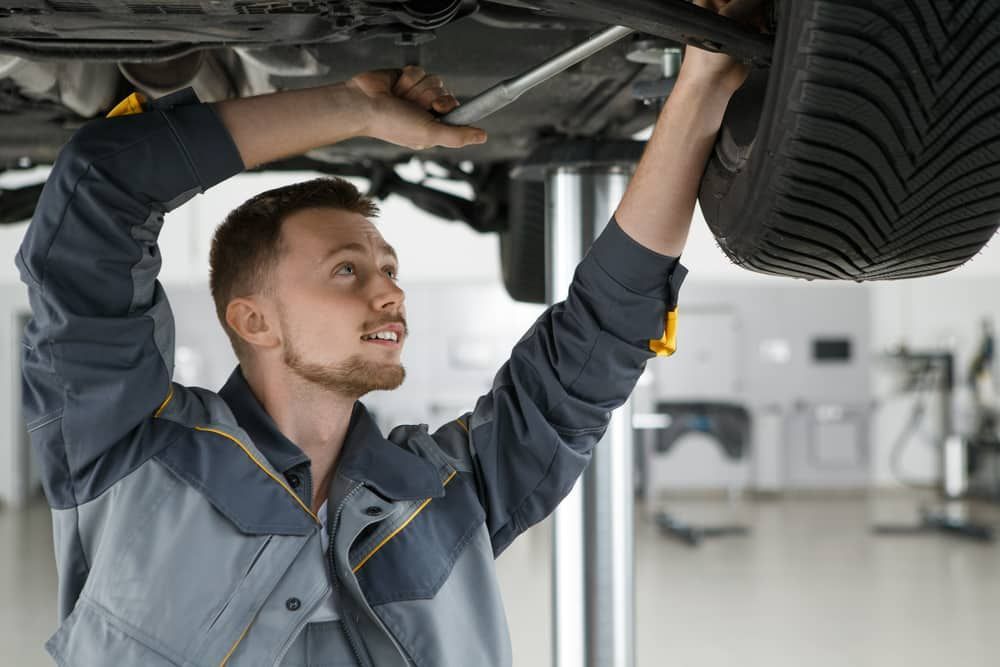 A Man Is Working Under A Car In A Garage — Automotive Repair Centre In Garbutt, QLD