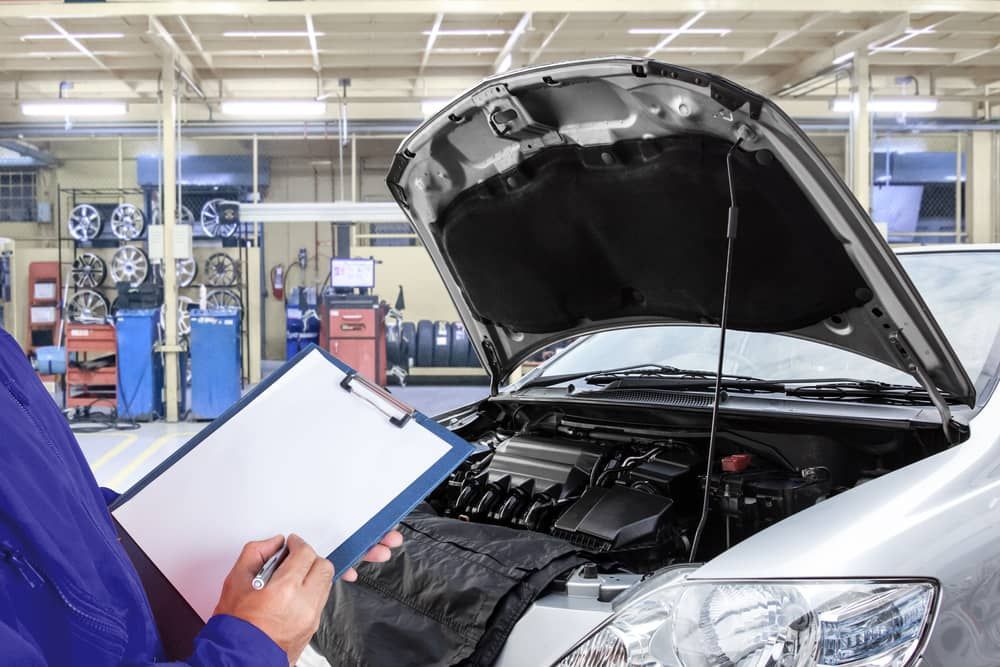 A Mechanic Is Looking At A Clipboard In Front Of A Car In A Garage — Automotive Repair Centre In Garbutt, QLD