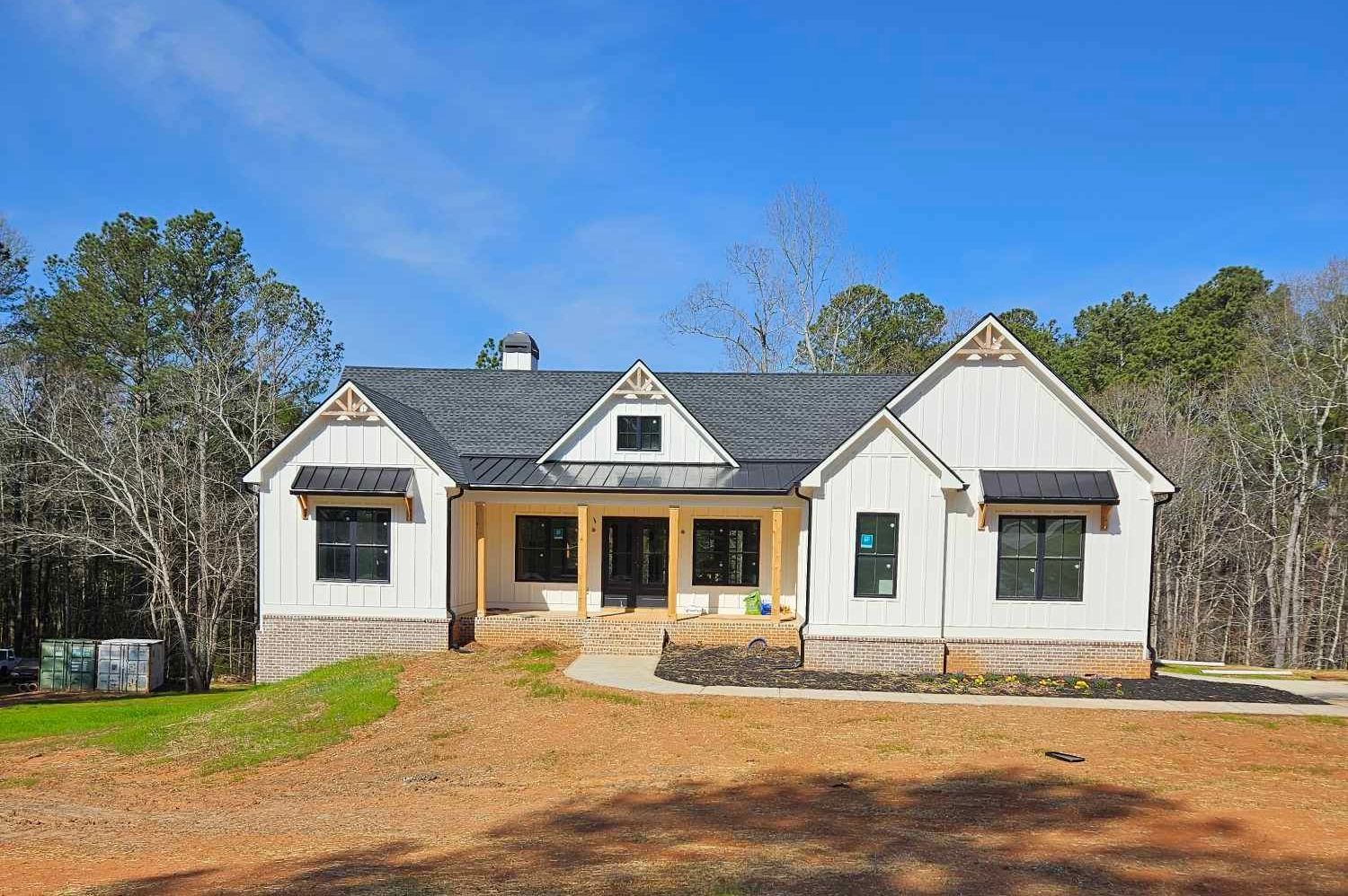 A white house with a black roof is sitting on top of a dirt field.