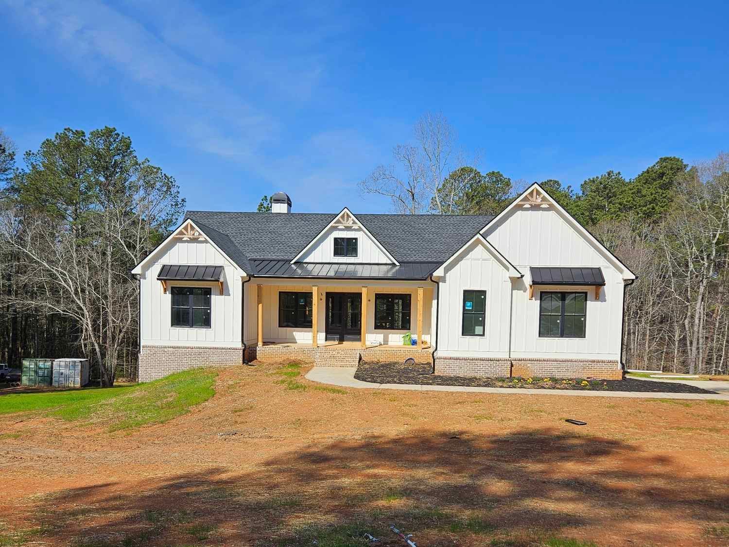 A white house with a gray roof is sitting on top of a dirt field.