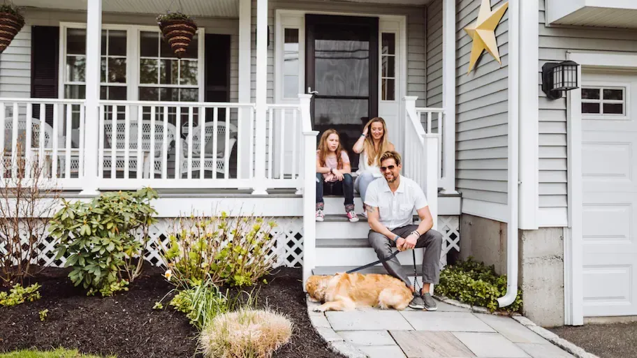 A family is sitting on the porch of their house with a dog.
