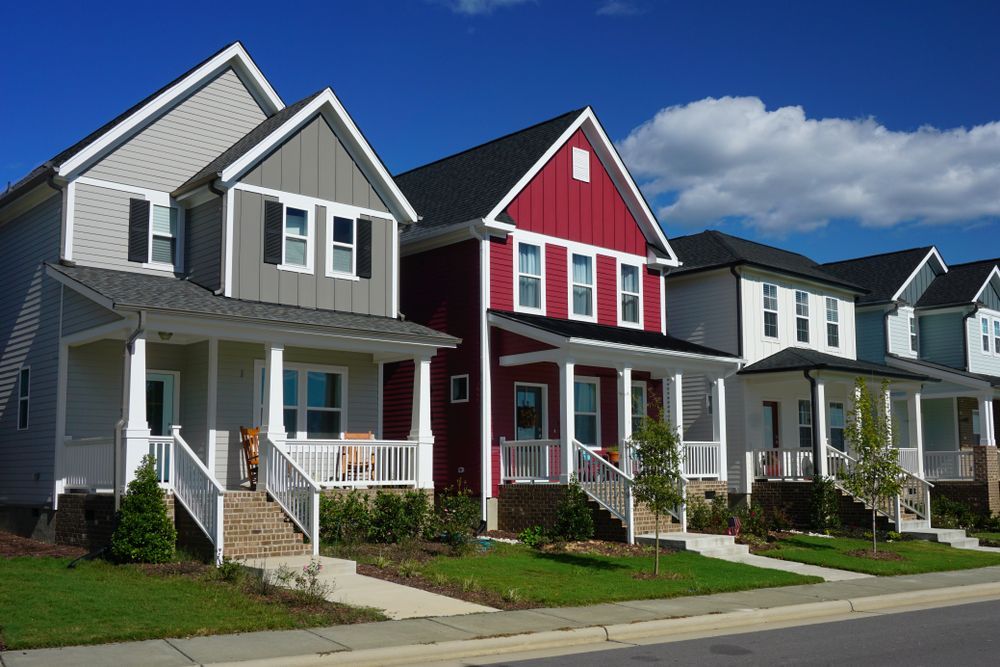 Row of modern two-story houses with front porches, various colors, blue sky.