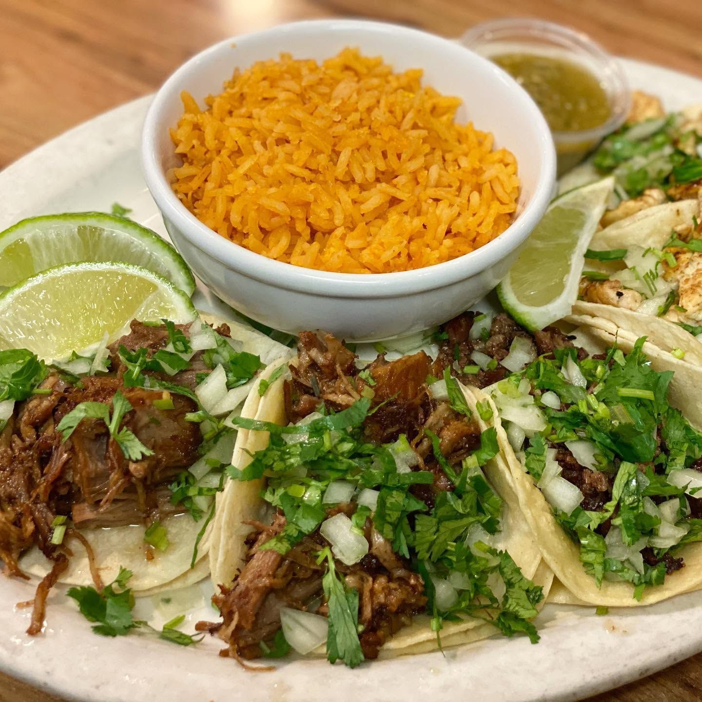 Plate of tacos with cilantro, onions, lime wedges, and a bowl of orange rice