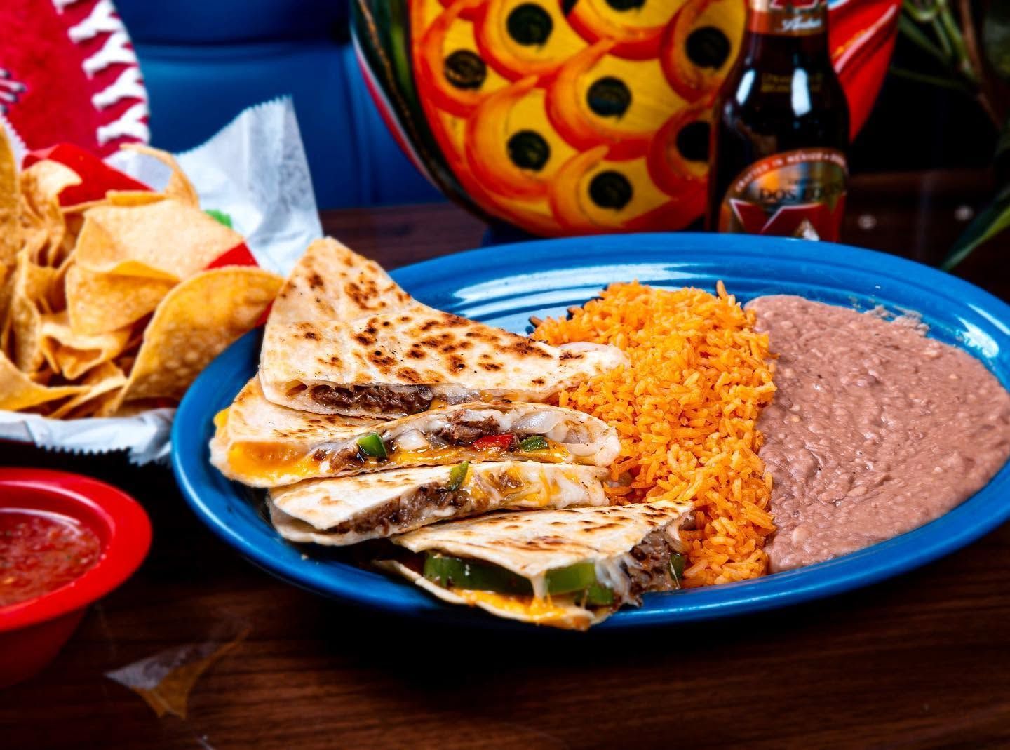 Platter of quesadilla slices with rice, refried beans, salsa, and tortilla chips on a blue plate