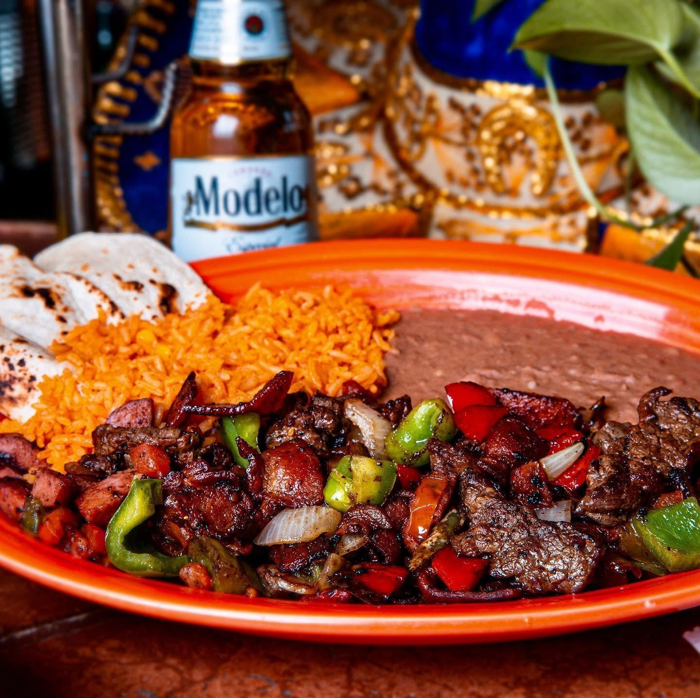 Plate of Mexican food with rice, beans, and sautéed peppers beside a Modelo beer bottle